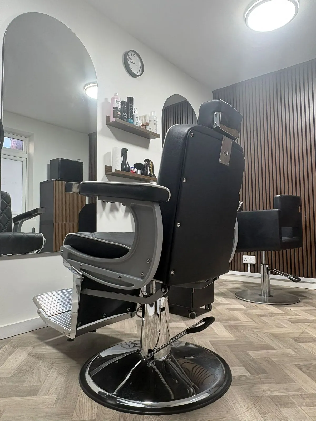 The Hair Aesthetics Club hair studio — two styling chairs, a tall arched mirror and a daylit window over a herringbone floor